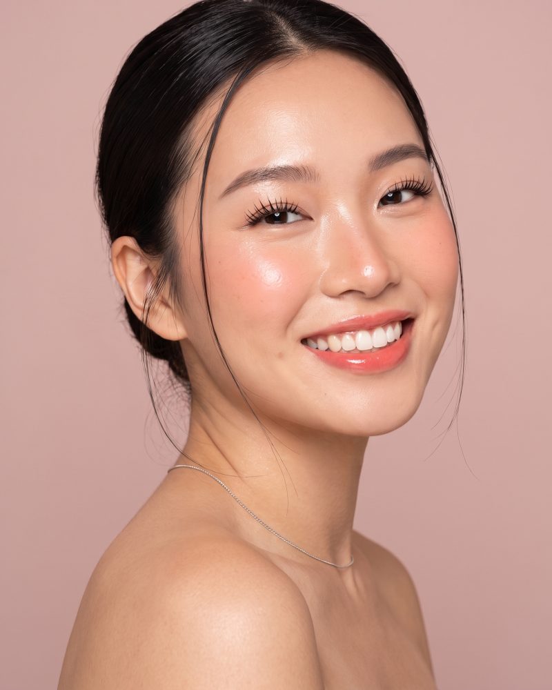 A client laughing, shot straight on against a dusty rose background.